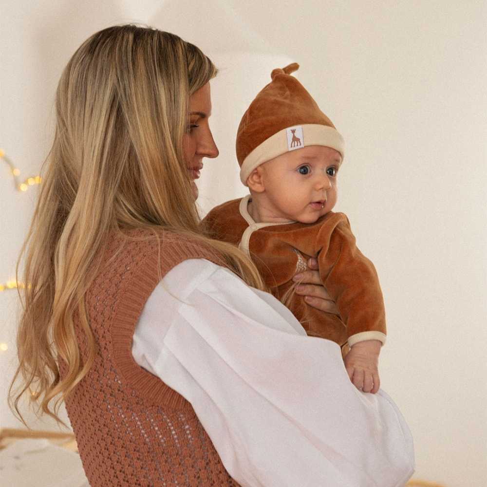 Baby with camel Sophie the giraffe bonnet in mom's arms