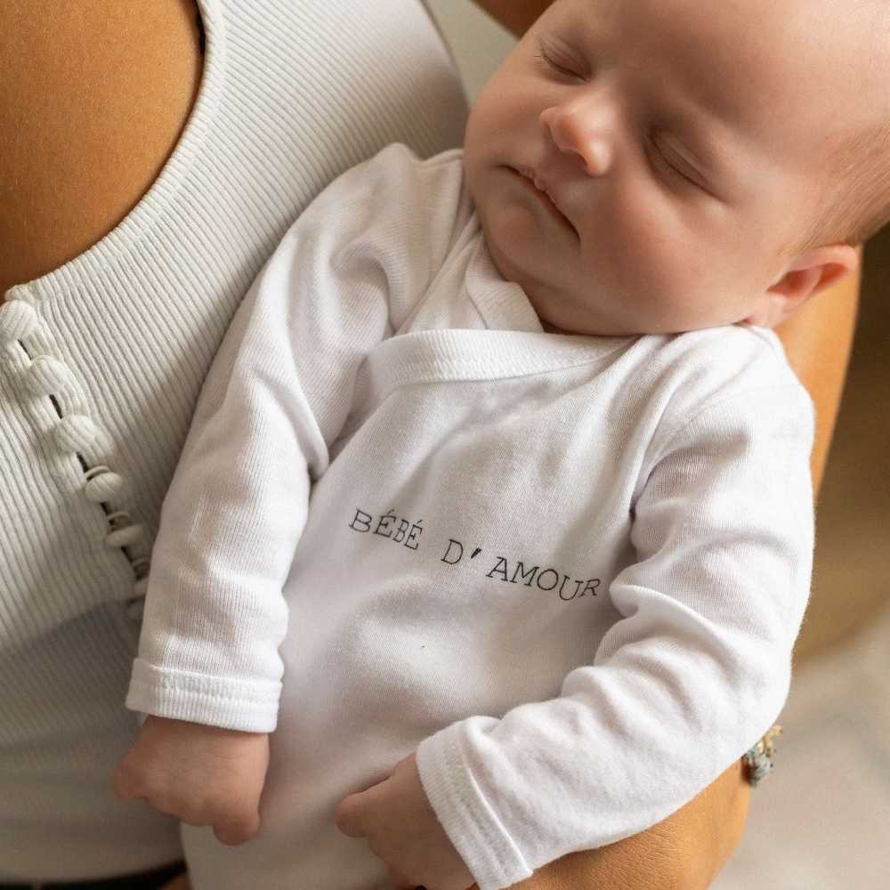 bebé llevando el body Trois kilos sept en los brazos de su mamá