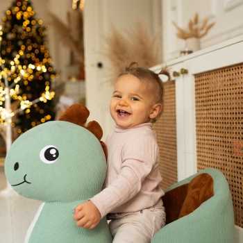 Baby auf seiner Dino-Schaukel am Fuß des Tannenbaums