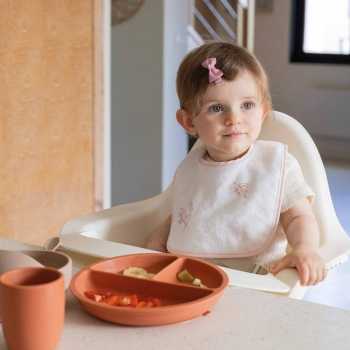 bebé en la mesa con su babero blanco y flores rosas