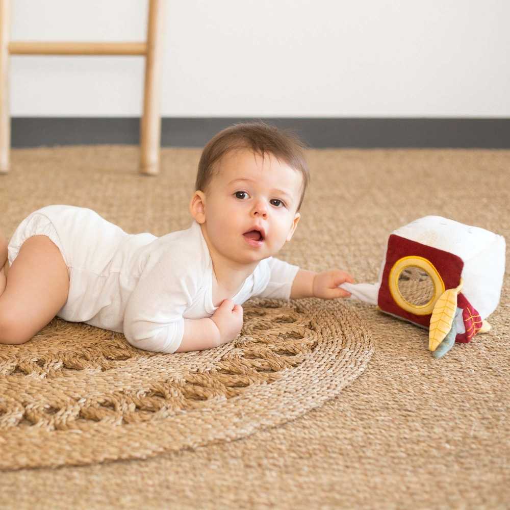 Bébé sur tapis qui joue avec son cube sensoriel.
