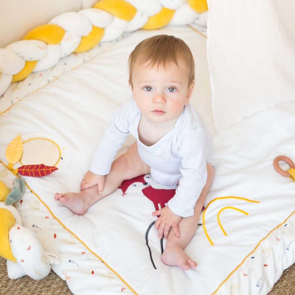 Petite fille assise sur son tapis d'éveil entouré de la tresse décorative
