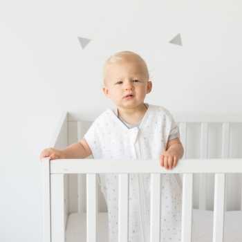 Baby steht in seinem Bett mit Sommerschlafsack