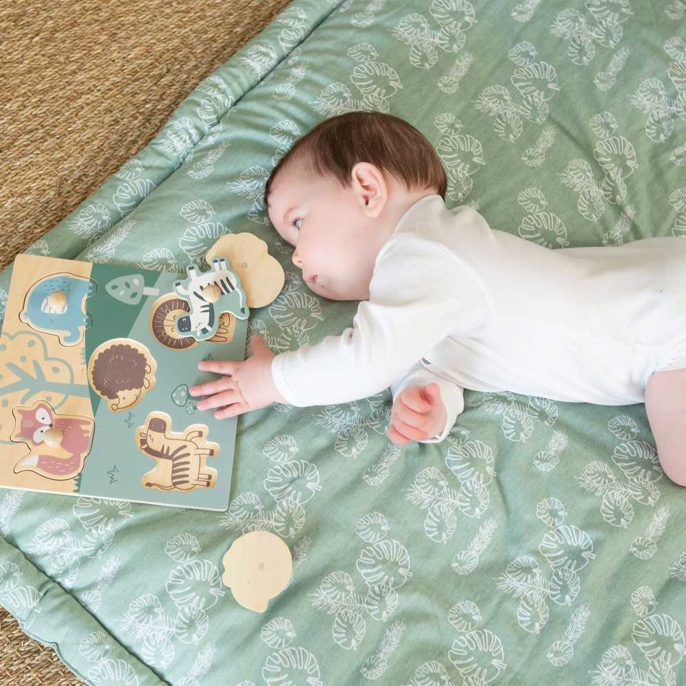 Bébé qui joue avec son puzzle en bois sur son tapis d'éveil feuilles