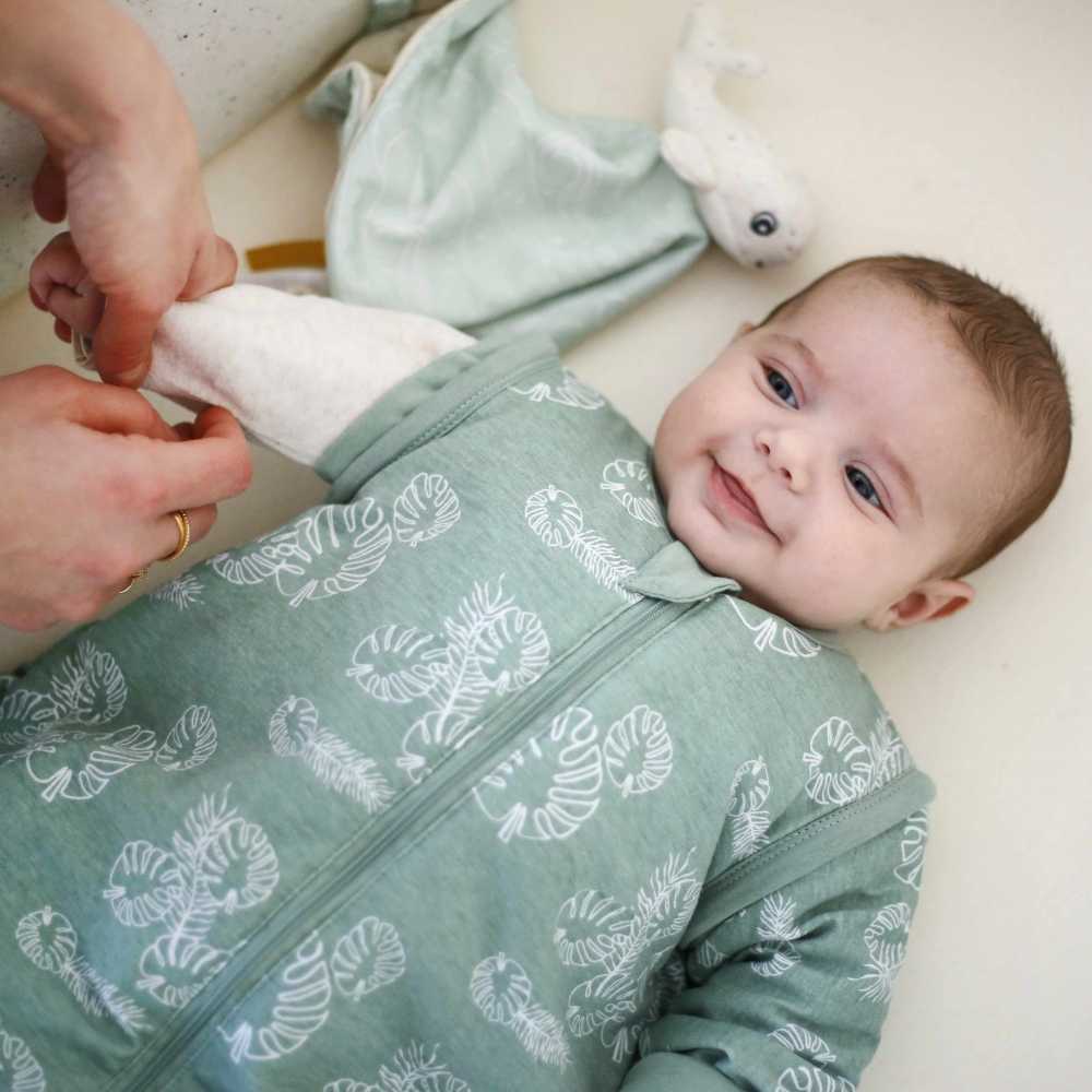 Baby lächelt, während Mama die Ärmel seines grünen Schlafsacks löst