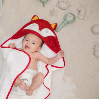 Babymeisje met badjas liggend in het zand.