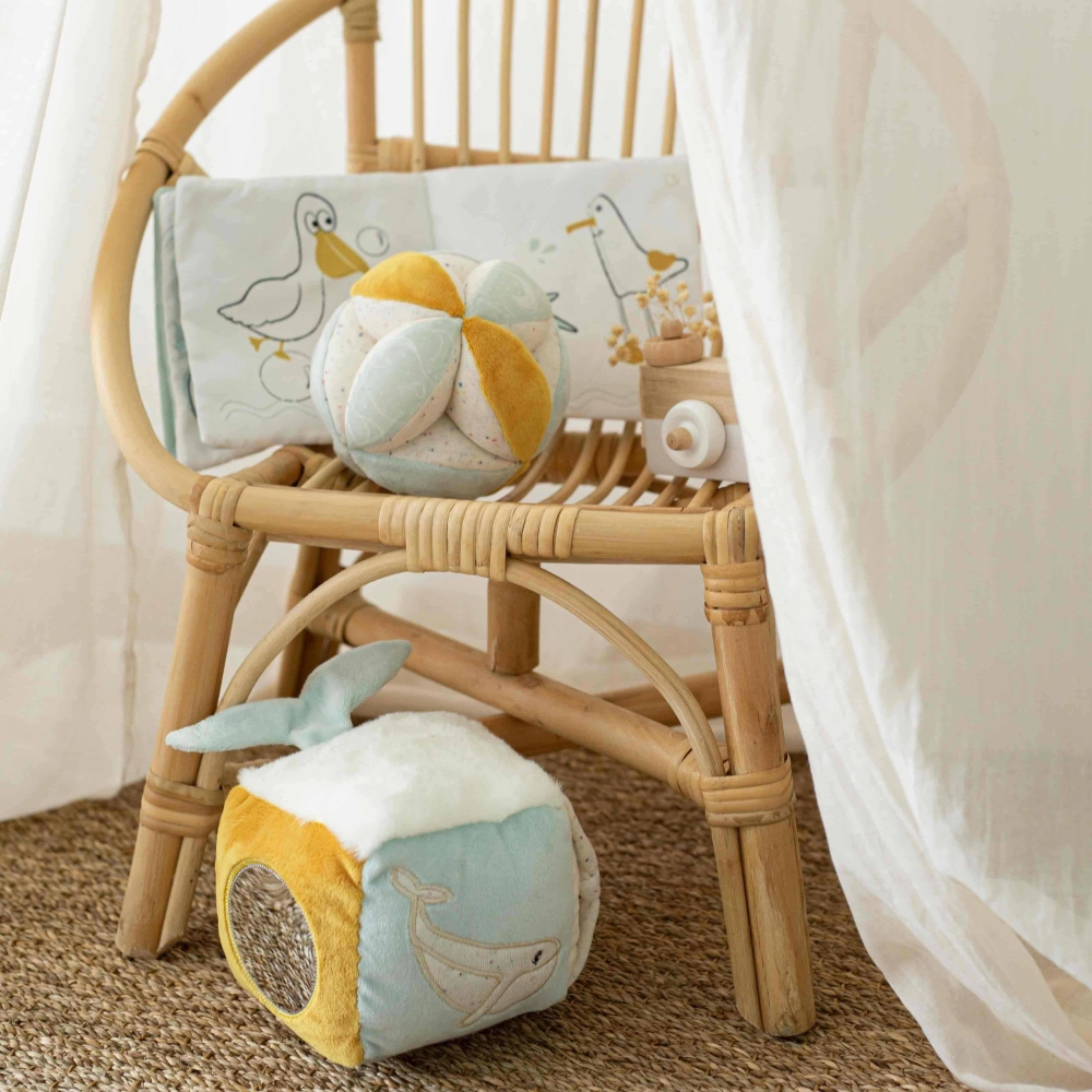 Sensorische kubus op de grond met ander babyspeelgoed uit de collectie op een rieten stoel