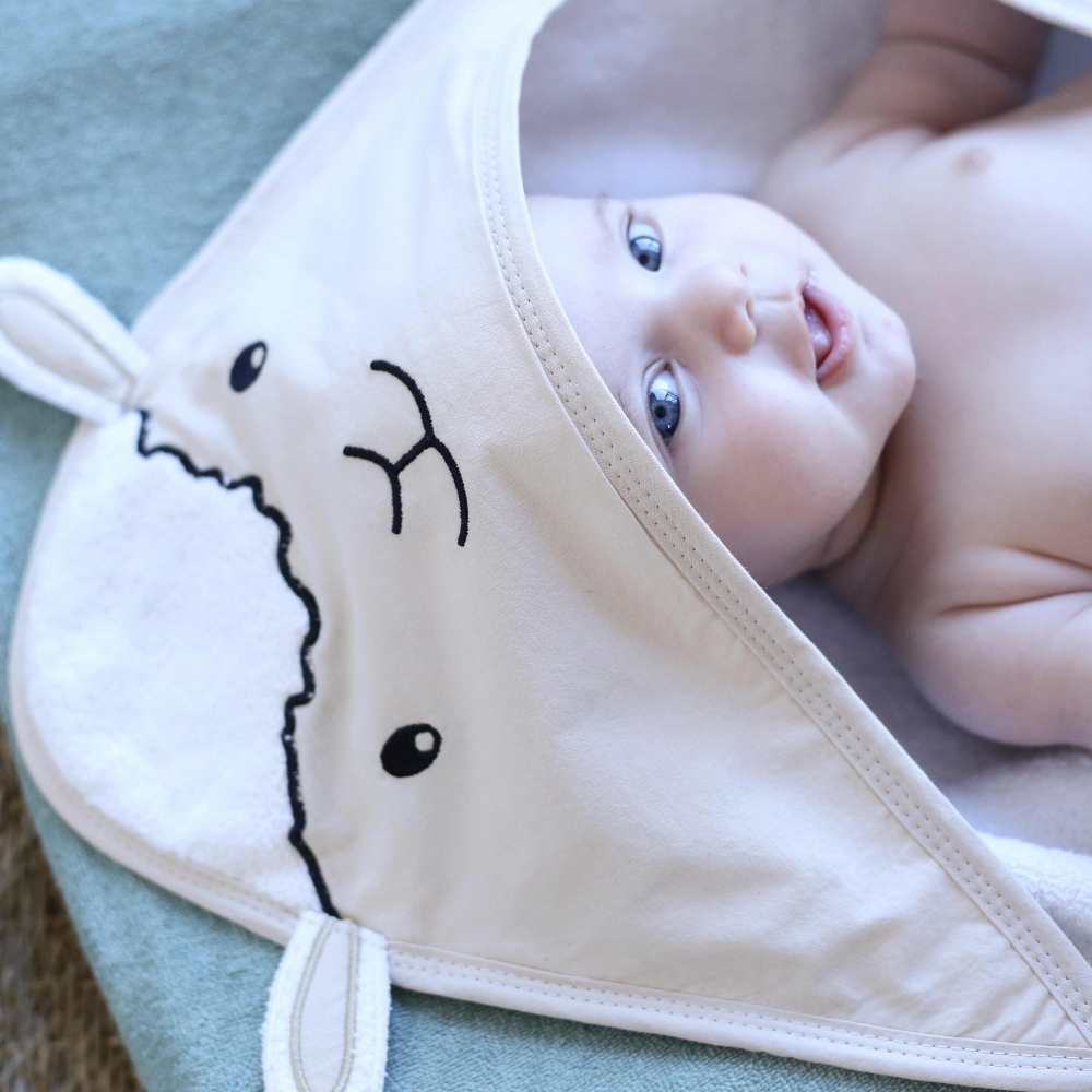 Baby, das in seinem mit kleinem Schaf dekorierten Baby-Bademantel lacht