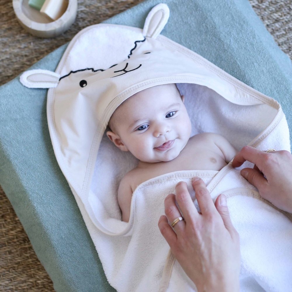 Mama, die ihr Baby mit dem beigen Bademantel mit kleinen Schafohren abtrocknet