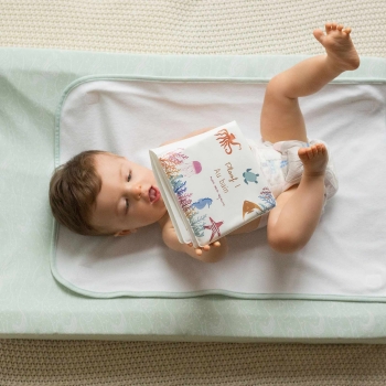 Baby die met zijn badboekje speelt liggend in luier op zijn aankleedkussen